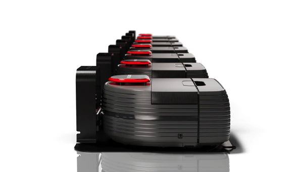 Row of black and gray robotic vacuum cleaners with red accents lined up on charging stations.
