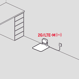 A device labeled 2G/LTE-M is plugged into a wall outlet near a desk with drawers.