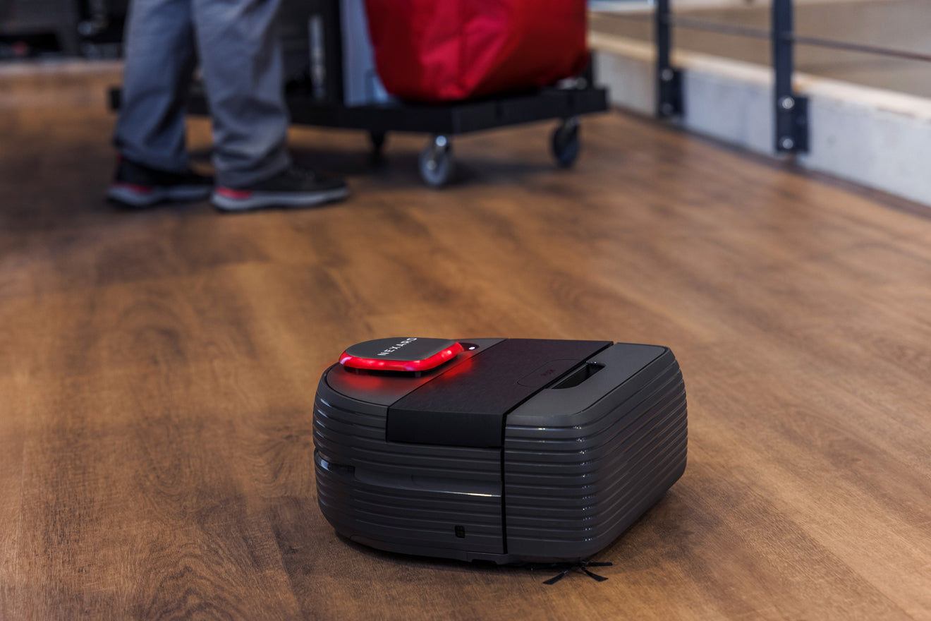 A robot vacuum cleaner on a wooden floor with a person standing in the background.