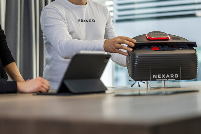 Two people interact with a Nexaro device on a table next to a tablet in a modern office setting.