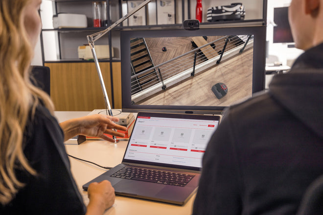Two people look at a computer and monitor displaying security camera footage and a security dashboard.