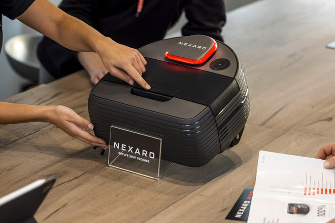 Two people interact with a Nexaro robotic device on a wooden table at a product demonstration.