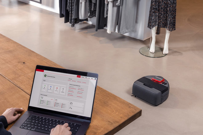 A sales assistant in a clothing store controls the Nexaro robot vacuum cleaner fleet via the Nexaro HUB on a laptop.