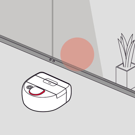 A robot vacuum approaches a glass wall with a red sensor beam reflected ahead.