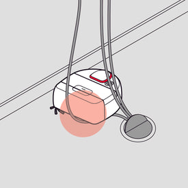 A robot vacuum tangled in cords near a wall and an electrical outlet.