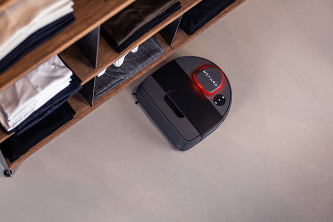 A Nexaro robot vacuum cleaner next to an open shelf with clothes