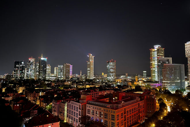 Night cityscape with illuminated skyscrapers and buildings under a clear sky, viewed from above.
