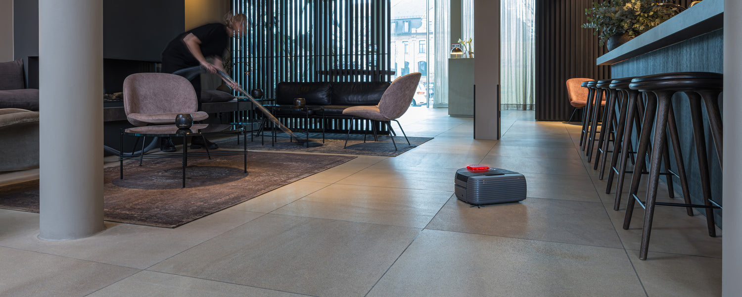 A person vacuums a modern living room with tiled floors and stylish furniture.