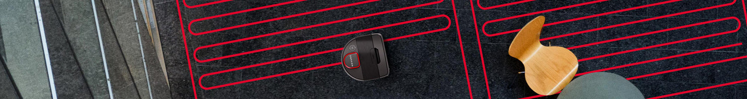 Top view of a robot vacuum cleaning a dark carpet with red lines, next to a wooden chair and table.