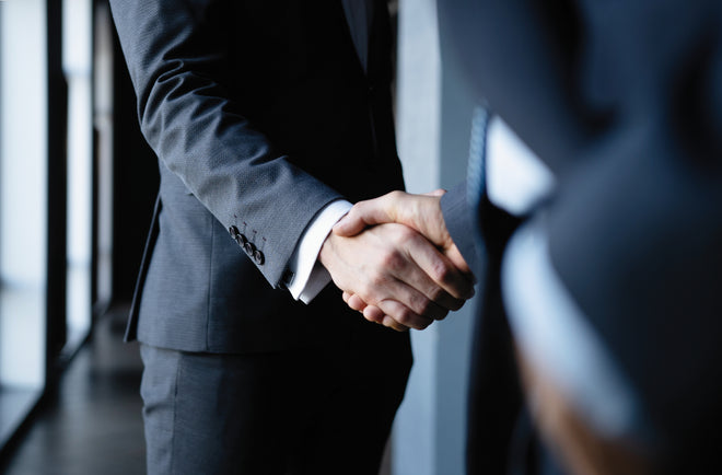 Two people in business suits shaking hands in an office setting.