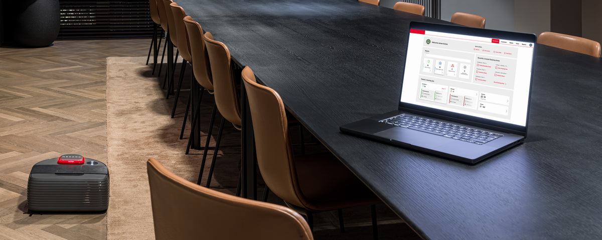 A laptop on a conference table and a small wheeled robot on the floor nearby.