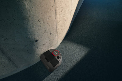 A robot vacuum cleaner cleaning near a curved concrete wall on a carpeted floor.
