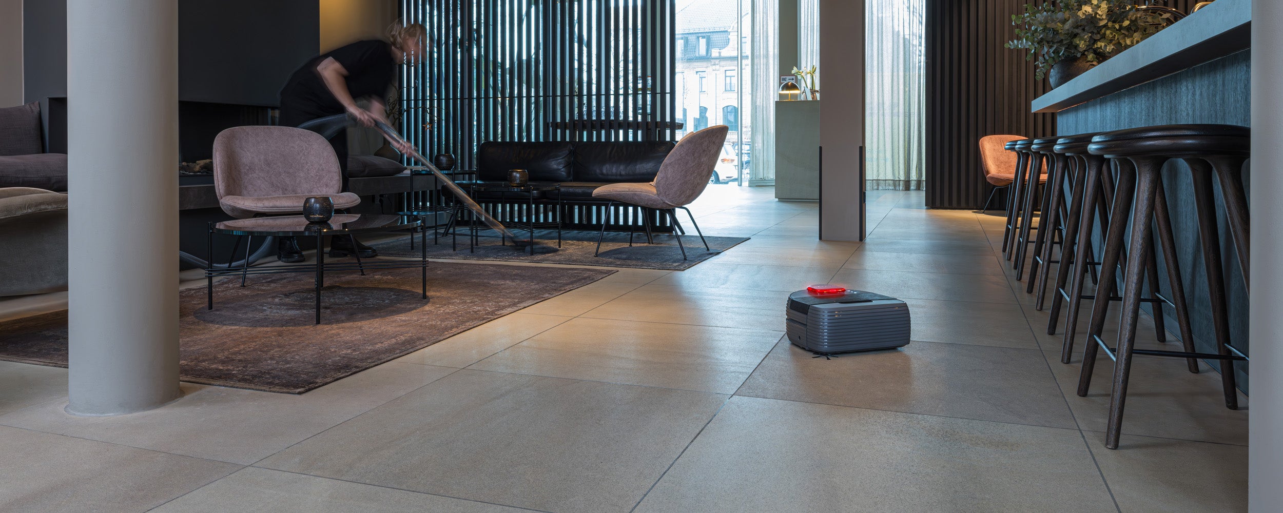 A person vacuums a modern living room with tiled floors and stylish furniture.